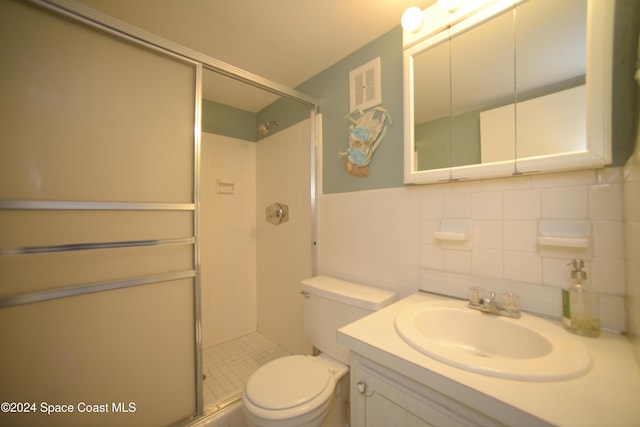 bathroom featuring vanity, a shower with door, toilet, tile walls, and tasteful backsplash