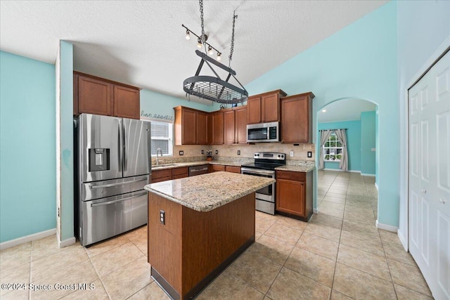 kitchen with appliances with stainless steel finishes, light stone counters, a textured ceiling, a kitchen island, and hanging light fixtures