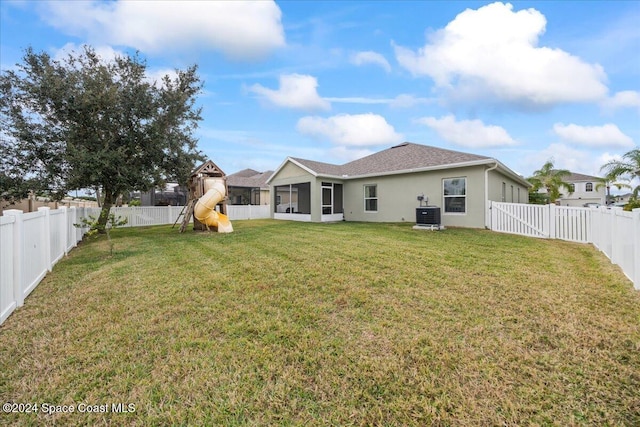 rear view of property featuring a playground, a sunroom, central air condition unit, and a lawn