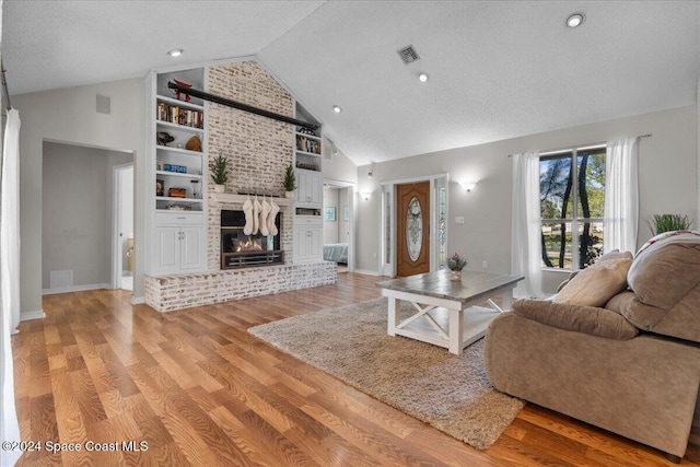 living room with a brick fireplace, a textured ceiling, high vaulted ceiling, and light hardwood / wood-style flooring