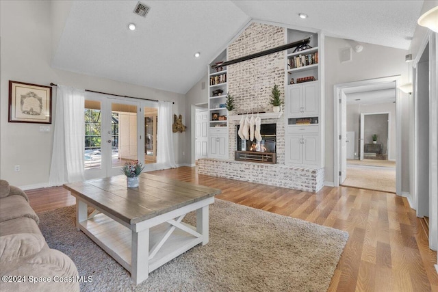 living room with french doors, high vaulted ceiling, light hardwood / wood-style floors, and a brick fireplace