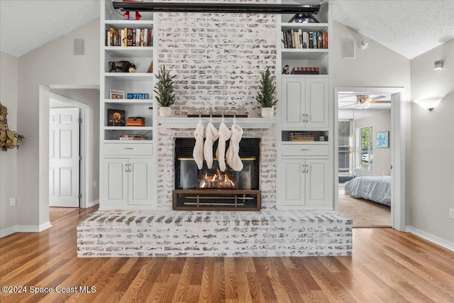 living room with ceiling fan, built in features, a textured ceiling, a fireplace, and light wood-type flooring