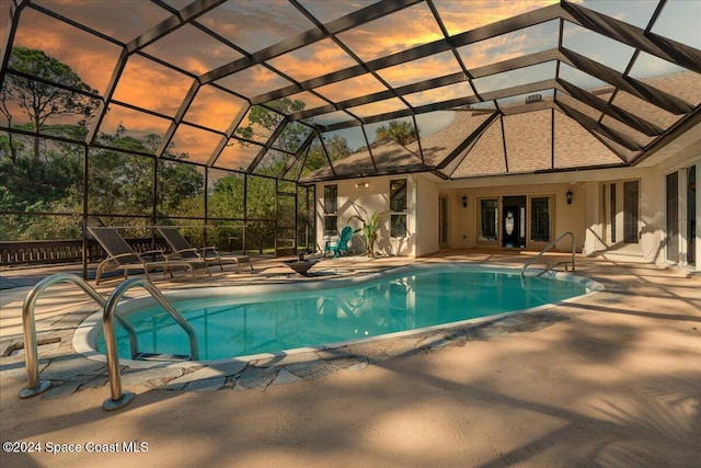 pool at dusk featuring a patio and glass enclosure