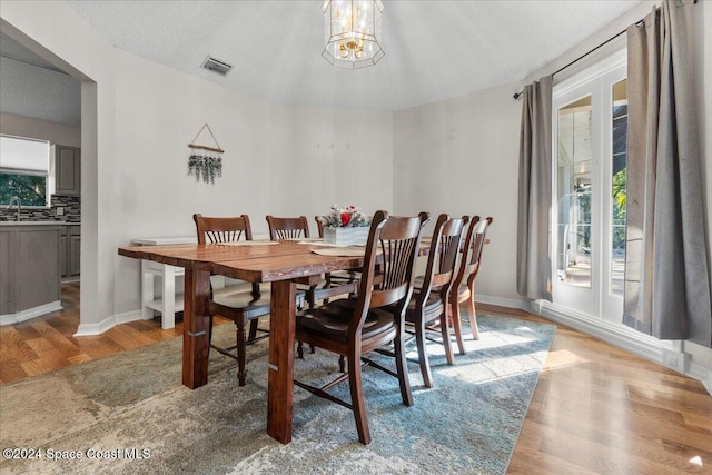 dining area with sink, light hardwood / wood-style flooring, a textured ceiling, and a notable chandelier