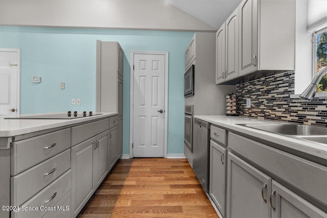 kitchen with appliances with stainless steel finishes, light wood-type flooring, sink, gray cabinets, and lofted ceiling