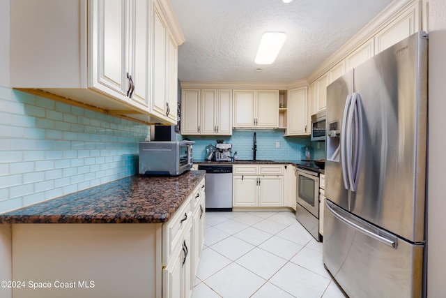 kitchen featuring tasteful backsplash, dark stone counters, stainless steel appliances, sink, and light tile patterned flooring