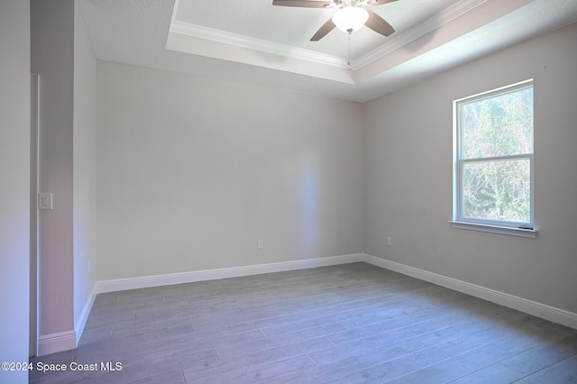 empty room with wood-type flooring, ornamental molding, and a tray ceiling