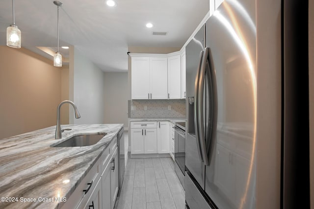 kitchen featuring white cabinets, appliances with stainless steel finishes, light stone counters, and sink