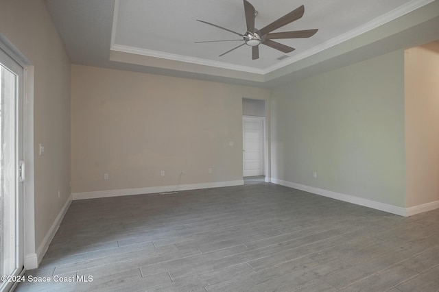 empty room featuring light wood-type flooring, a tray ceiling, ceiling fan, and ornamental molding