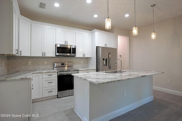 kitchen with white cabinets, decorative light fixtures, an island with sink, and appliances with stainless steel finishes