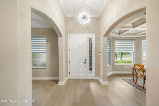 entrance foyer with coffered ceiling, crown molding, a chandelier, beam ceiling, and light hardwood / wood-style floors