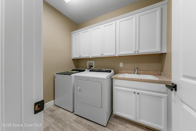 laundry area with sink, light wood-type flooring, cabinets, washing machine and clothes dryer, and a textured ceiling