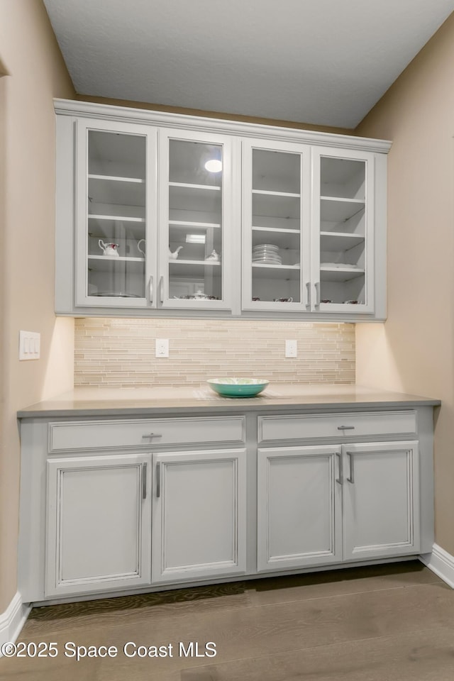 bar with tasteful backsplash, white cabinets, and light hardwood / wood-style flooring