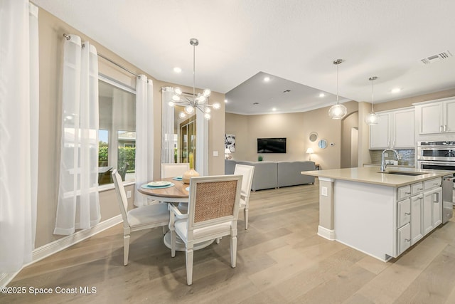 dining area featuring light wood-type flooring, sink, and a notable chandelier