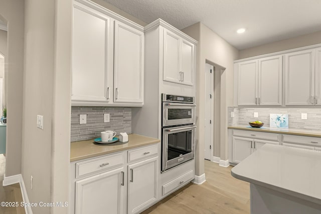 kitchen with white cabinetry, stainless steel double oven, backsplash, and light wood-type flooring