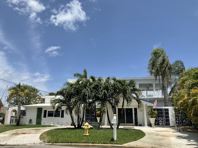 view of front of property featuring driveway, stucco siding, a balcony, and a front yard