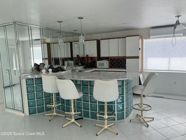 kitchen featuring a wall unit AC, white microwave, plenty of natural light, a kitchen breakfast bar, and a textured ceiling