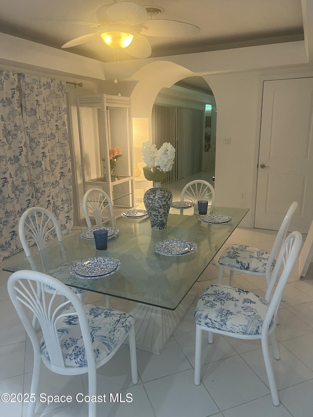 tiled dining space with arched walkways and a ceiling fan