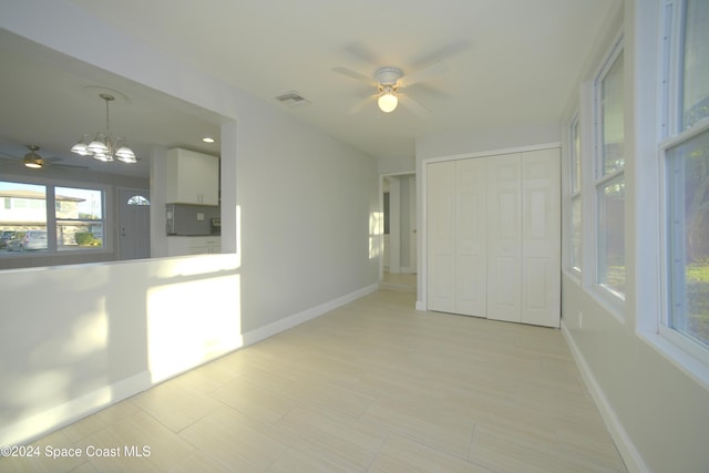 tiled empty room with ceiling fan with notable chandelier