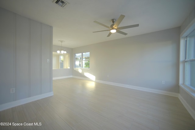 spare room with light wood-type flooring and ceiling fan with notable chandelier