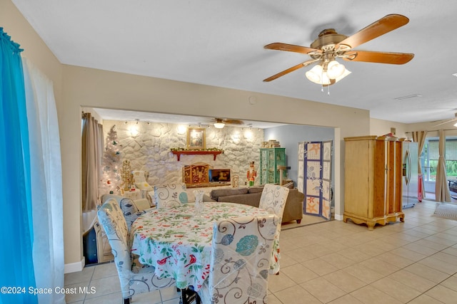 dining room featuring ceiling fan, light tile patterned flooring, and a fireplace