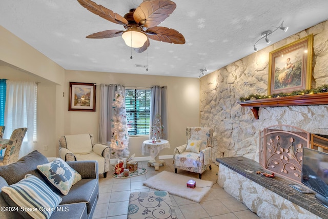 living room featuring ceiling fan, track lighting, a textured ceiling, a fireplace, and light tile patterned floors