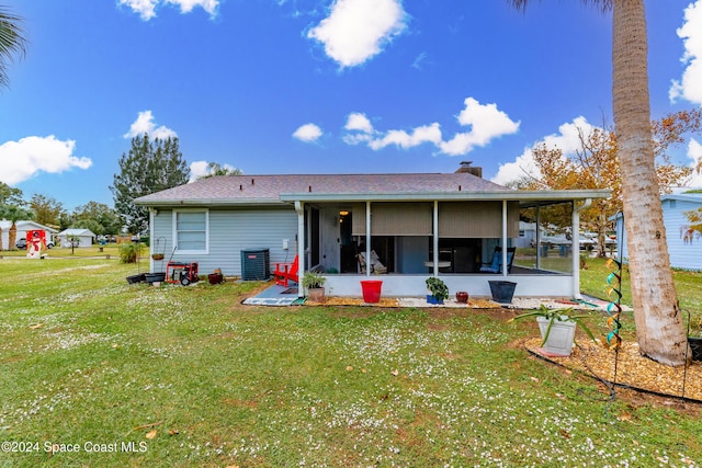 rear view of house with a sunroom, central AC unit, and a lawn