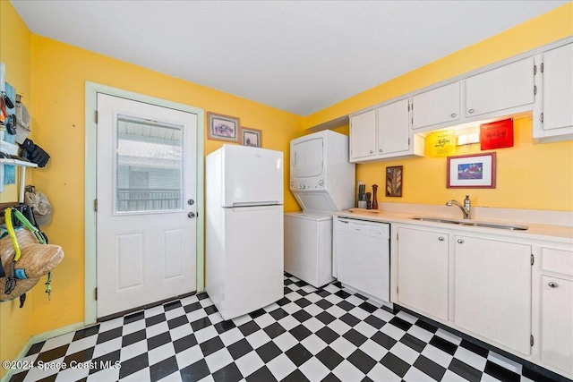 kitchen featuring white appliances, white cabinets, sink, stacked washing maching and dryer, and a textured ceiling