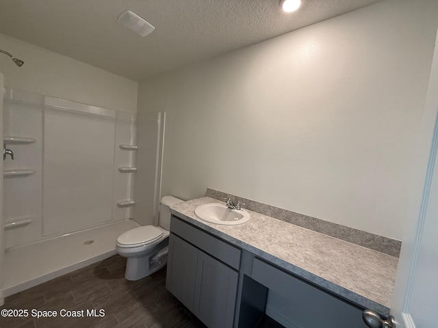 bathroom featuring a textured ceiling, vanity, toilet, and walk in shower