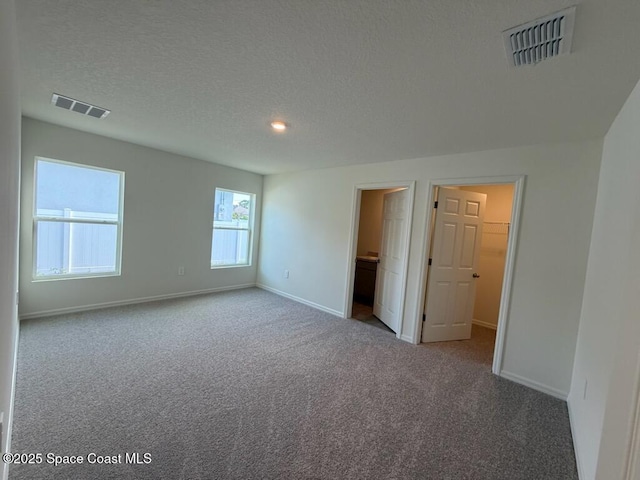 unfurnished bedroom with connected bathroom, a textured ceiling, a walk in closet, light carpet, and a closet