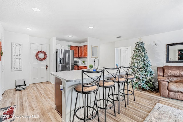 kitchen with a textured ceiling, stainless steel appliances, a kitchen island with sink, light hardwood / wood-style floors, and a breakfast bar area