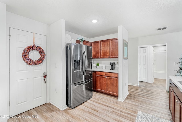 kitchen featuring stainless steel fridge, light wood-type flooring, and a textured ceiling