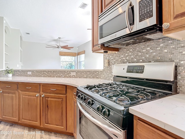 kitchen featuring ceiling fan, stainless steel appliances, tasteful backsplash, light stone counters, and light wood-type flooring