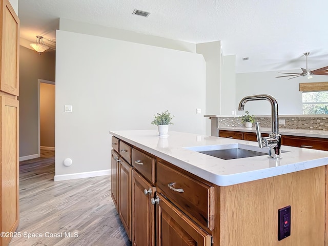 kitchen featuring a center island with sink, sink, ceiling fan, a textured ceiling, and light hardwood / wood-style floors