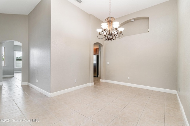 tiled spare room featuring high vaulted ceiling and an inviting chandelier