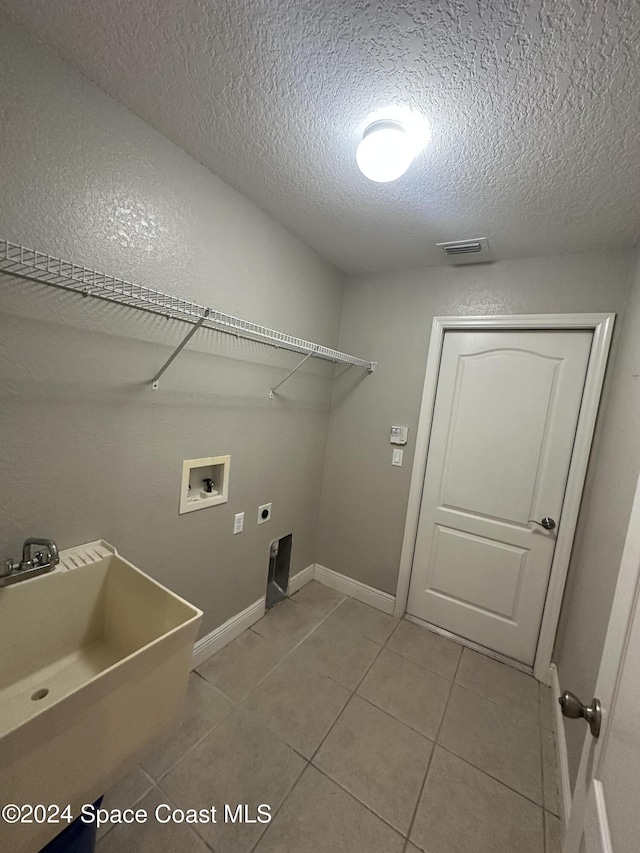 clothes washing area featuring washer hookup, a textured ceiling, electric dryer hookup, sink, and light tile patterned floors