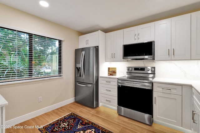 kitchen with decorative backsplash, white cabinetry, stainless steel appliances, and light hardwood / wood-style floors