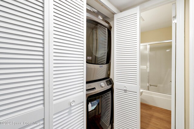 clothes washing area featuring hardwood / wood-style floors and stacked washing maching and dryer