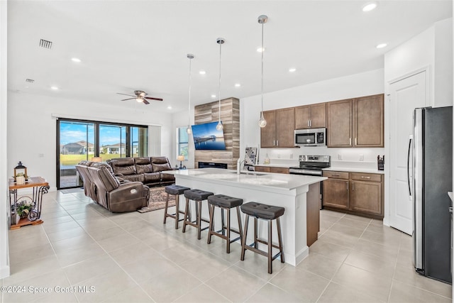 kitchen with ceiling fan, stainless steel appliances, an island with sink, pendant lighting, and a breakfast bar