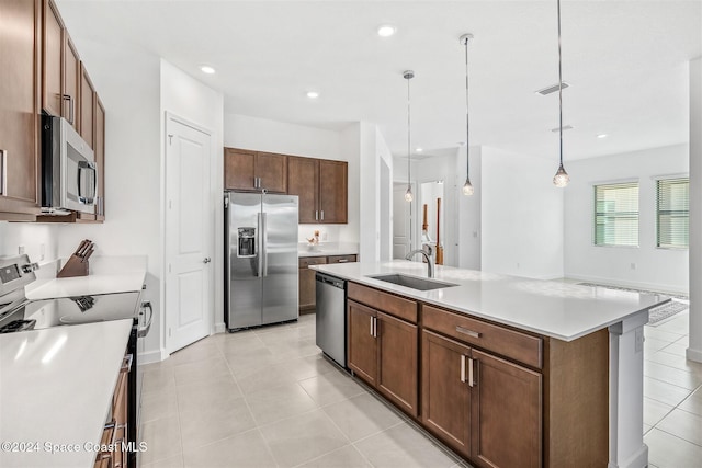 kitchen with sink, stainless steel appliances, an island with sink, pendant lighting, and light tile patterned floors