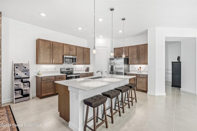 kitchen featuring a breakfast bar, stainless steel appliances, sink, decorative light fixtures, and an island with sink