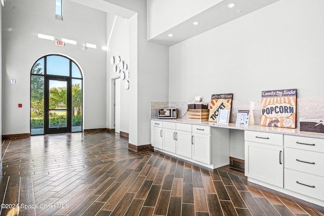 interior space featuring a high ceiling, dark hardwood / wood-style flooring, white cabinetry, and light stone counters