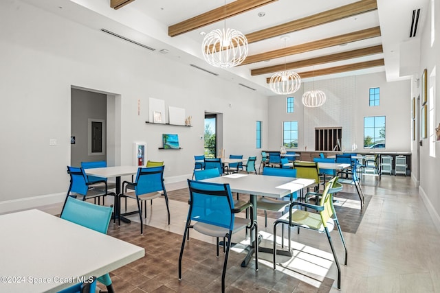 dining area featuring beam ceiling, a large fireplace, a chandelier, and a high ceiling