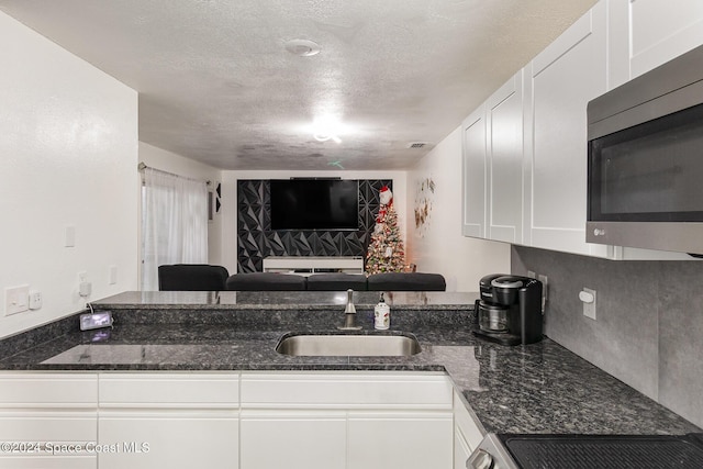 kitchen featuring white cabinets, dark stone counters, and sink