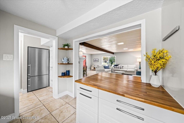 kitchen featuring stainless steel refrigerator, butcher block counters, beamed ceiling, light tile patterned flooring, and white cabinets