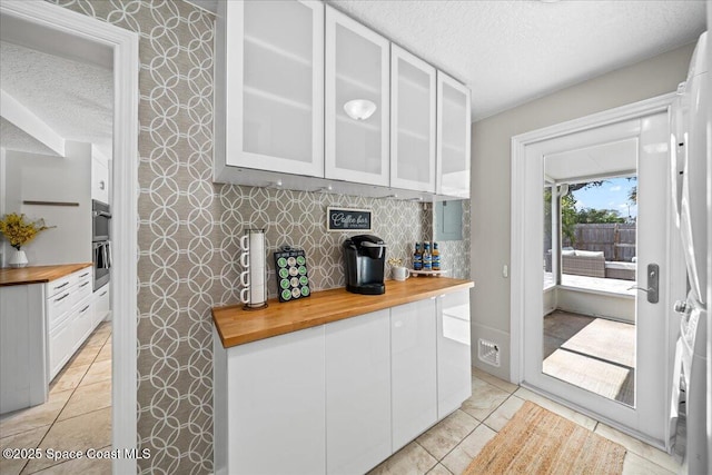 kitchen featuring white cabinets, a textured ceiling, butcher block counters, and light tile patterned flooring