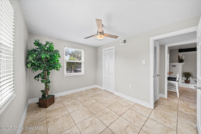 tiled spare room featuring ceiling fan, a textured ceiling, and a brick fireplace