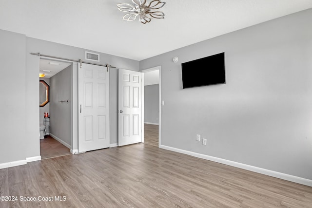 unfurnished bedroom with a barn door and light hardwood / wood-style floors