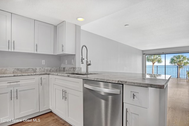 kitchen with light stone countertops, white cabinetry, sink, stainless steel dishwasher, and kitchen peninsula