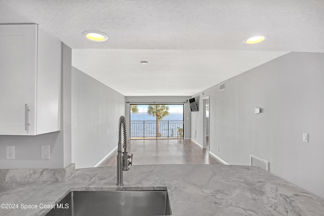 kitchen with a textured ceiling, white cabinetry, and sink